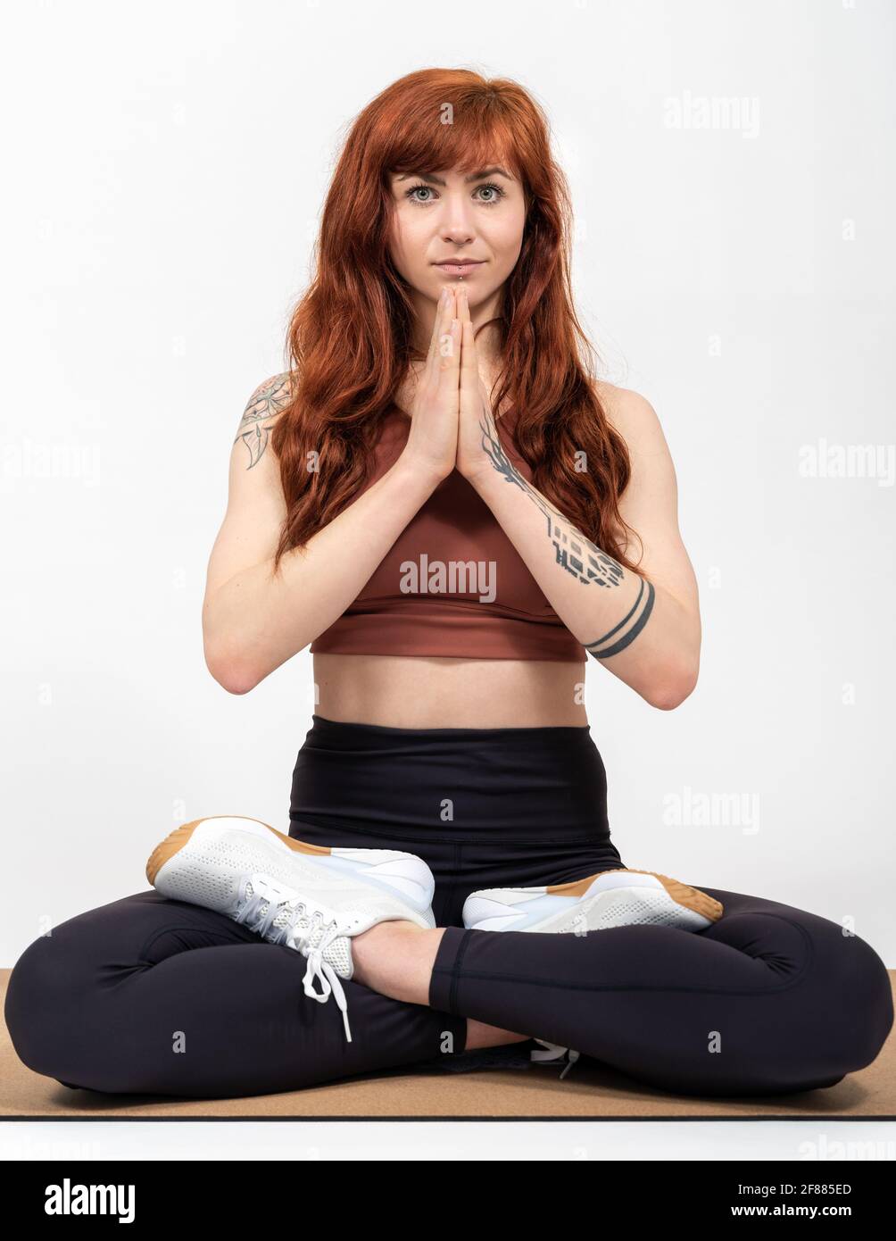 Portrait of a woman with red hair infront of white background in tailor seat folding hands Stock Photo