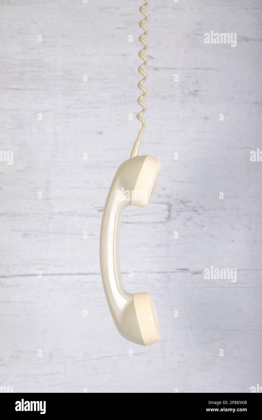 old telephone receiver hangs on the telephone cord in front of a gray