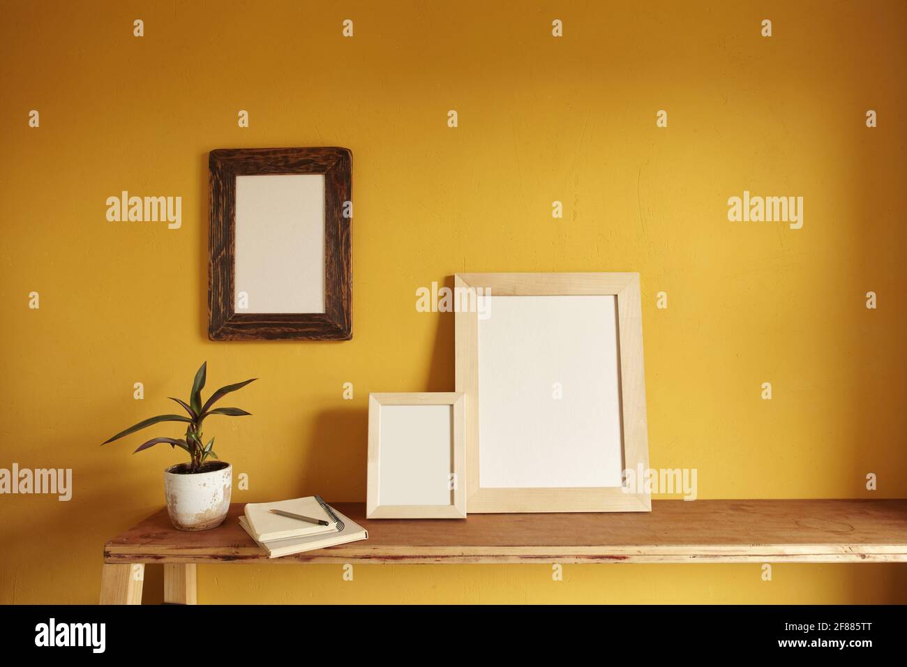 Wooden frames mockup. Flowerpot on a pile of books on an old wooden shelf. Composition on a yellow wall background Stock Photo