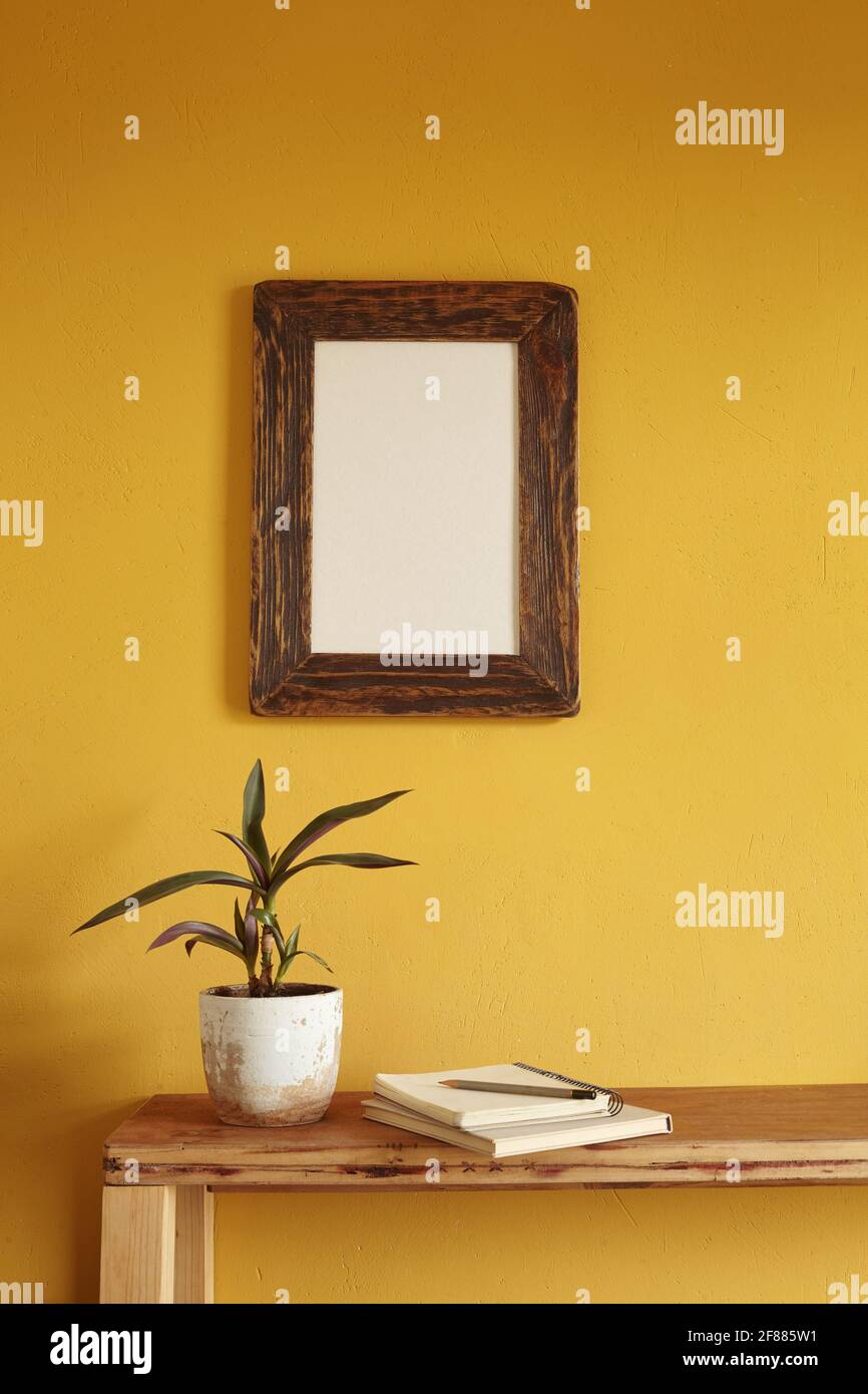 Wooden frame mockup. Flowerpot on a pile of books on an old wooden shelf. Composition on a yellow wall background Stock Photo