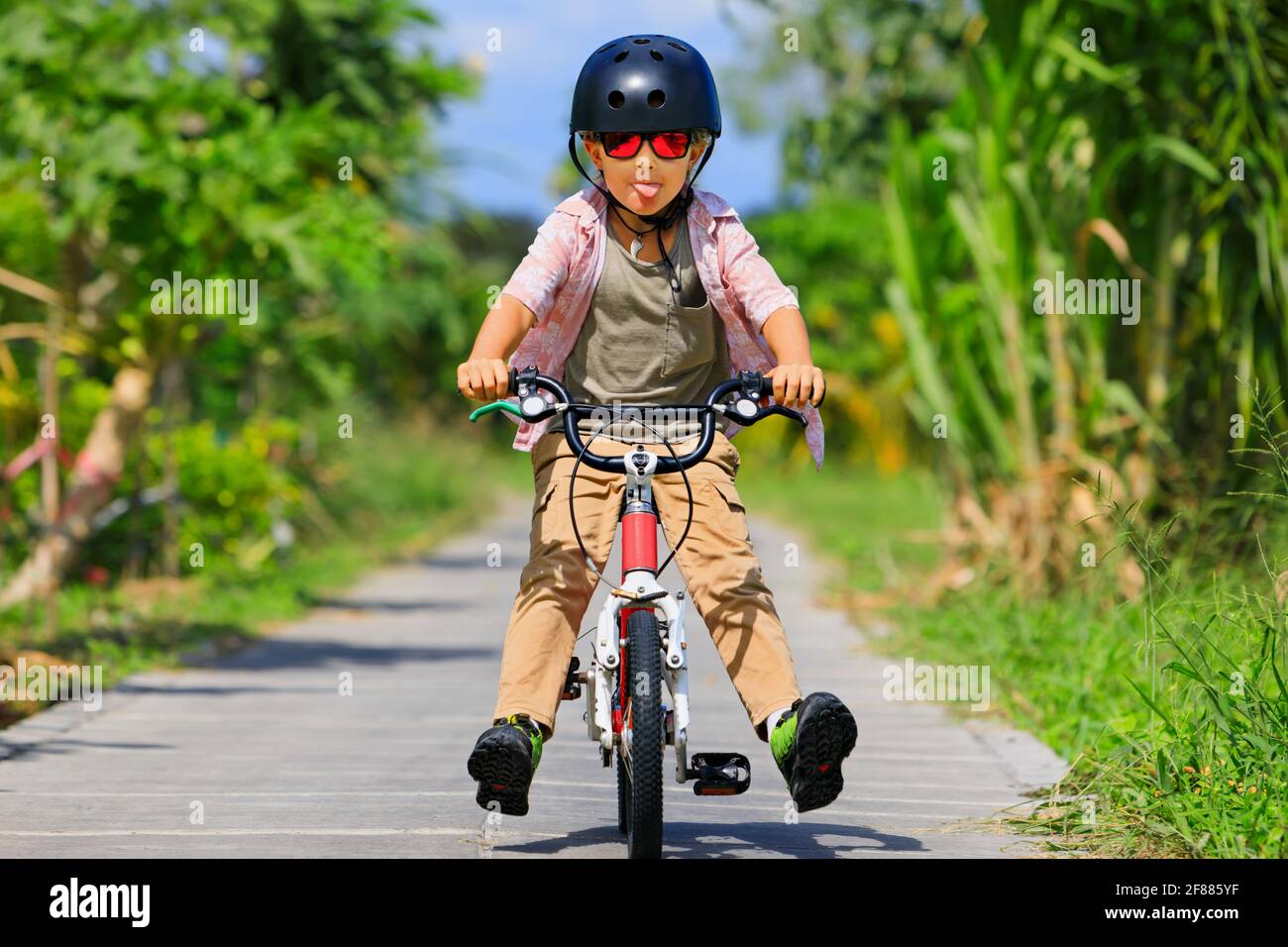 Country cycling walk. Young rider kid in helmet and sunglasses riding bicycle. Happy child have fun on empty trail. Active family lifestyle, sports, o Stock Photo