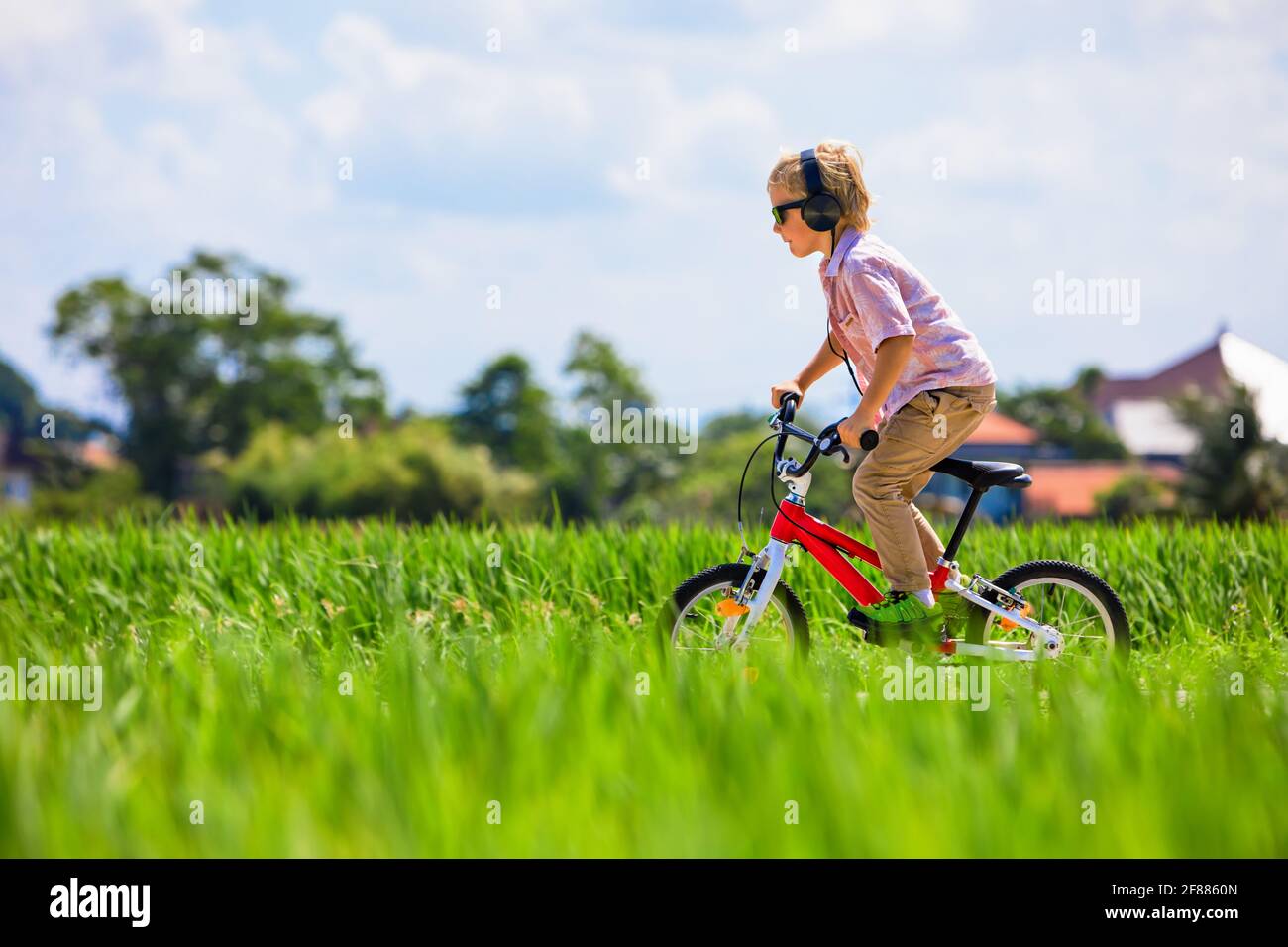 Country cycling walk. Young rider kid in headphones and sunglasses riding bicycle. Happy child have fun on field trail. Active family lifestyle, sport Stock Photo