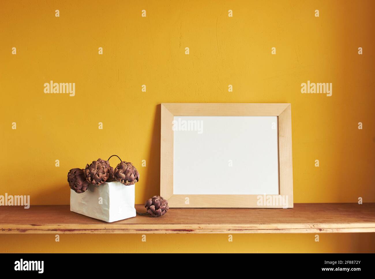 Wooden frames mockup. Dry decorative artichokes in a vase on an old wooden shelf. Composition on a yellow wall background Stock Photo