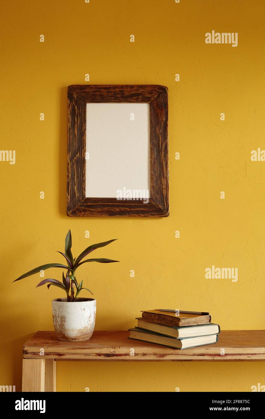 Wooden picture frame mockup. Flowerpot on a pile of books on an old wooden shelf. Composition on a yellow wall background Stock Photo