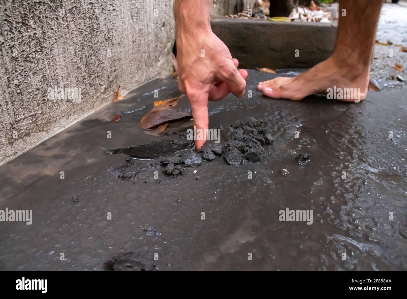 St. James, Barbados - April 11 2021: White man drags finger through wet volcanic ash from St. Vincent's Soufriere volcano eruption. Severe ash fall. Stock Photo