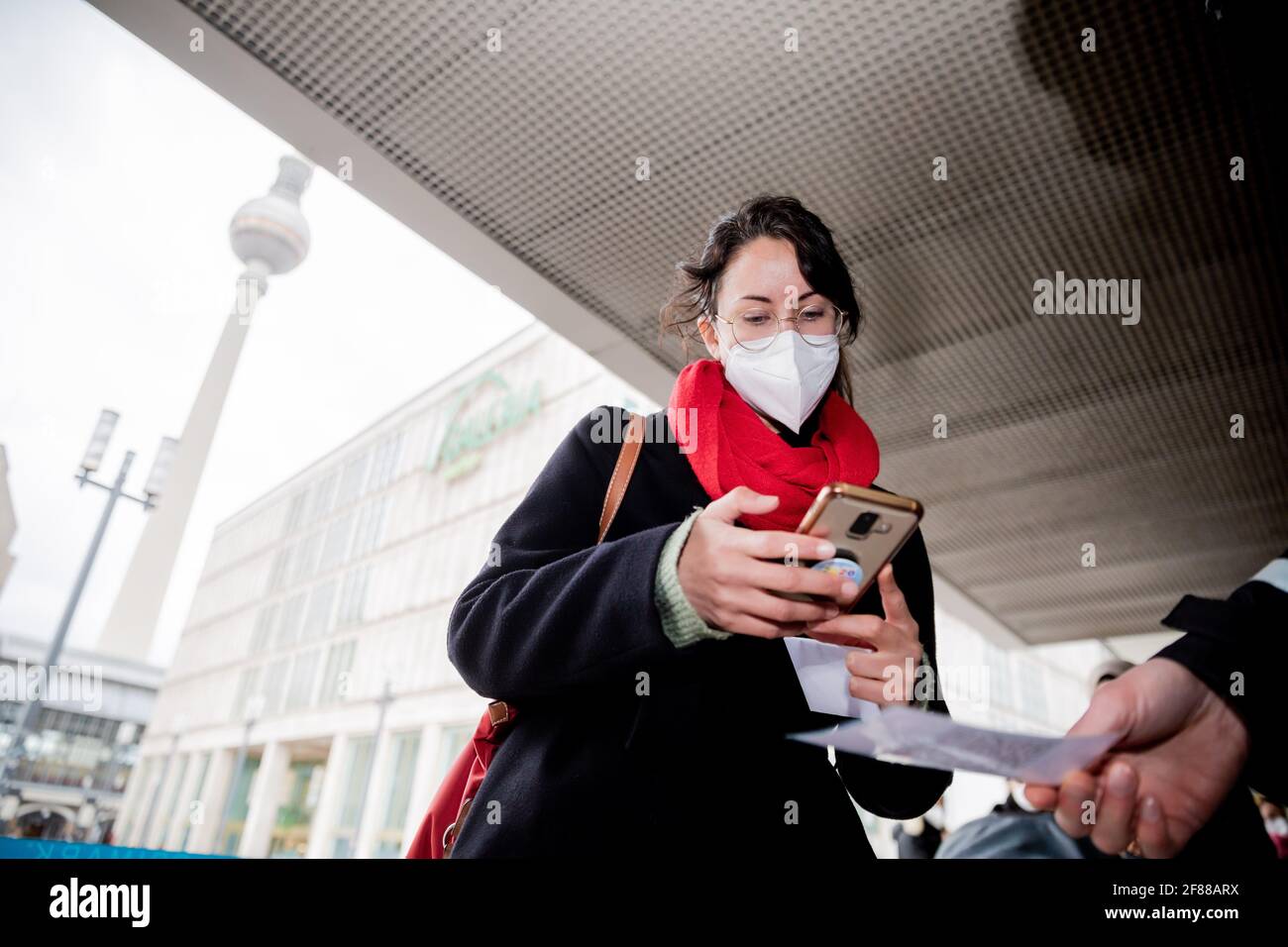 Berlin, Germany. 12th Apr, 2021. A customer scans a QR code at the entrance of a clothing store at Alexanderplatz in front of a security guard using the Luca app. The app is used to provide data for possible contact tracing. Credit: Christoph Soeder/dpa/Alamy Live News Stock Photo