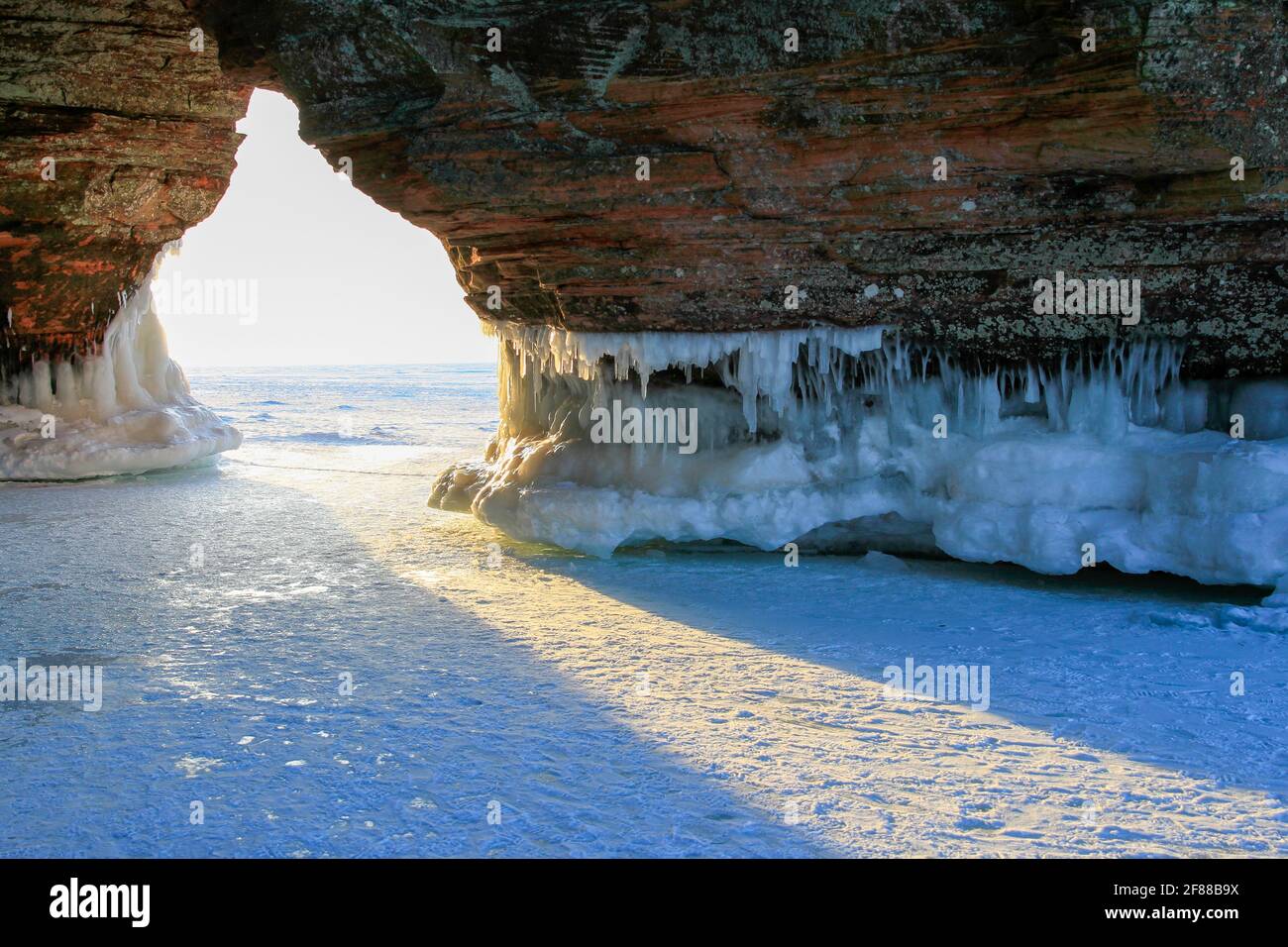 Light coming through entrance to ice cave with red cliffs, icicles and