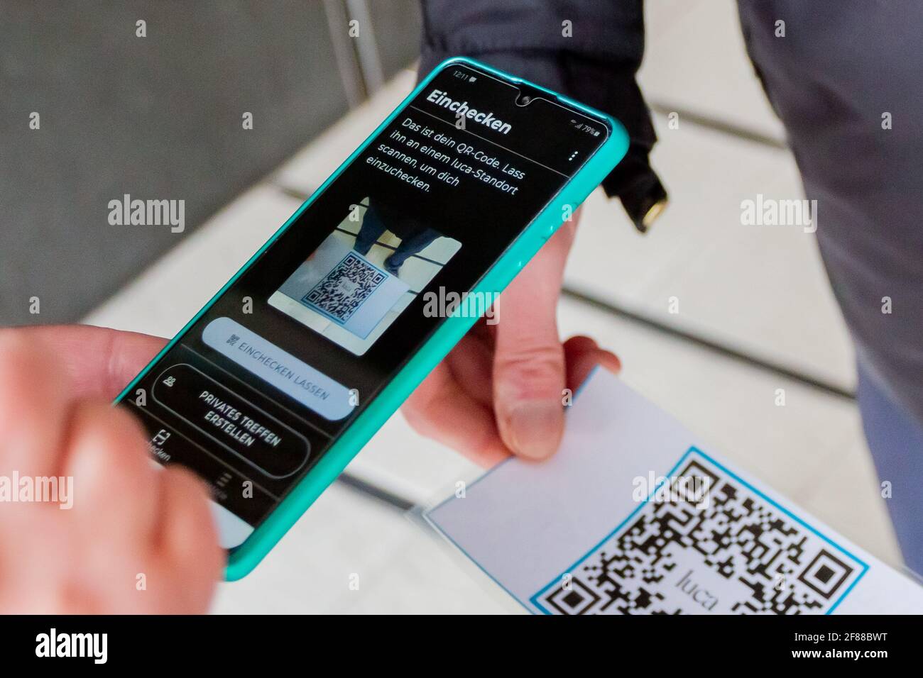 Berlin, Germany. 12th Apr, 2021. A person scans a QR code at the entrance of a clothing store at Alexanderplatz in front of a security guard using the Luca app. The app is used to provide data for possible contact tracing. Credit: Christoph Soeder/dpa/Alamy Live News Stock Photo