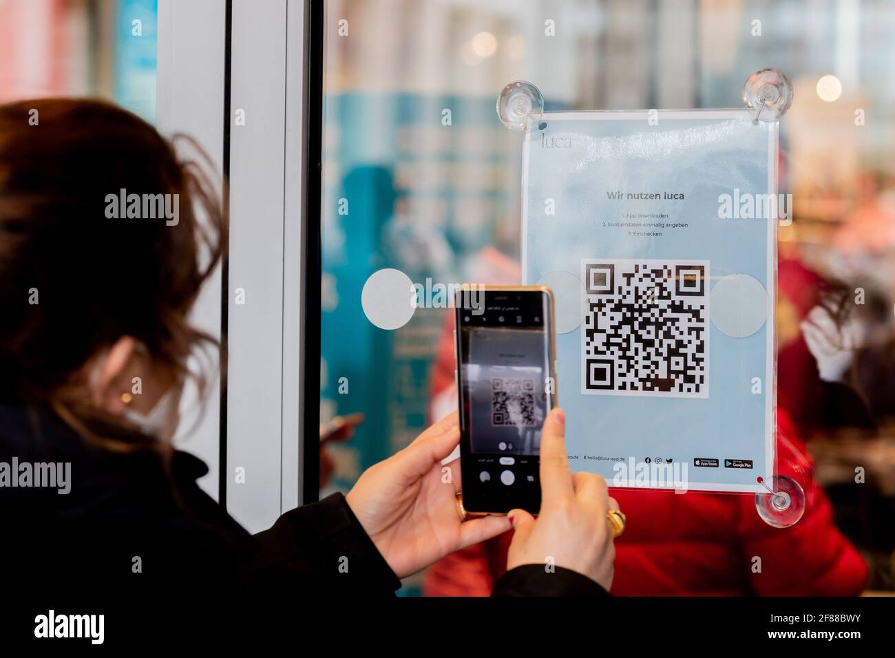Berlin, Germany. 12th Apr, 2021. A woman scans a QR code at the entrance of a clothing store at Alexanderplatz to download the Luca app. The app is used to provide data for possible contact tracing. Credit: Christoph Soeder/dpa/Alamy Live News Stock Photo
