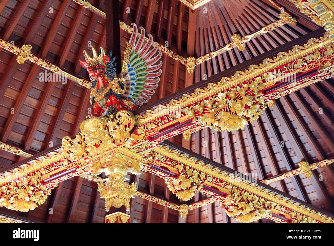 Traditional red wood decoration of roof inside building with carved dragon and gold detail in Bali, Indonesia Stock Photo