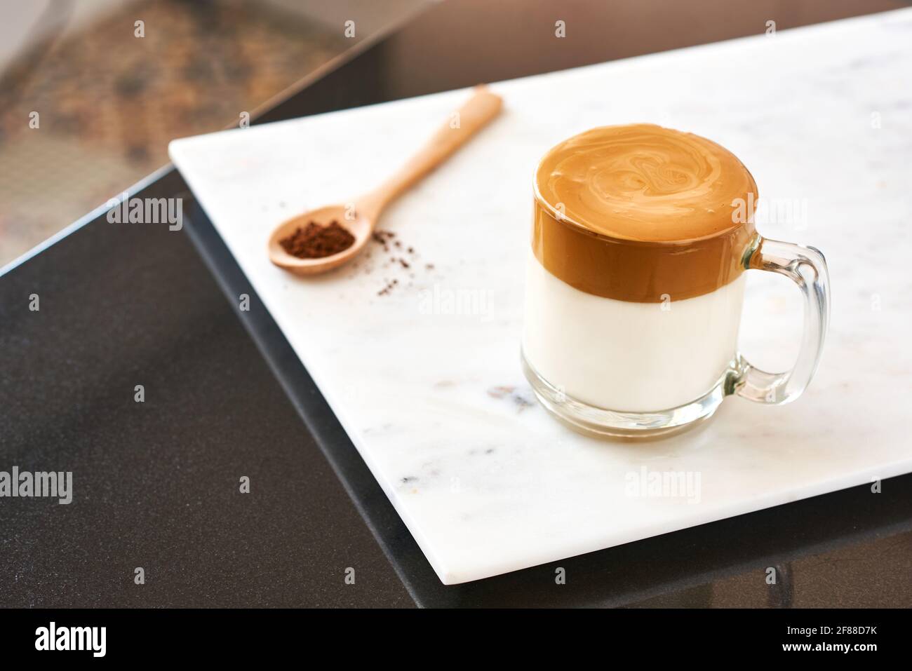 Dalgona coffee, fluffy creamy shake coffee in a transparent glass on a marble background next to a wooden spoon. Very popular in Korea. Stock Photo