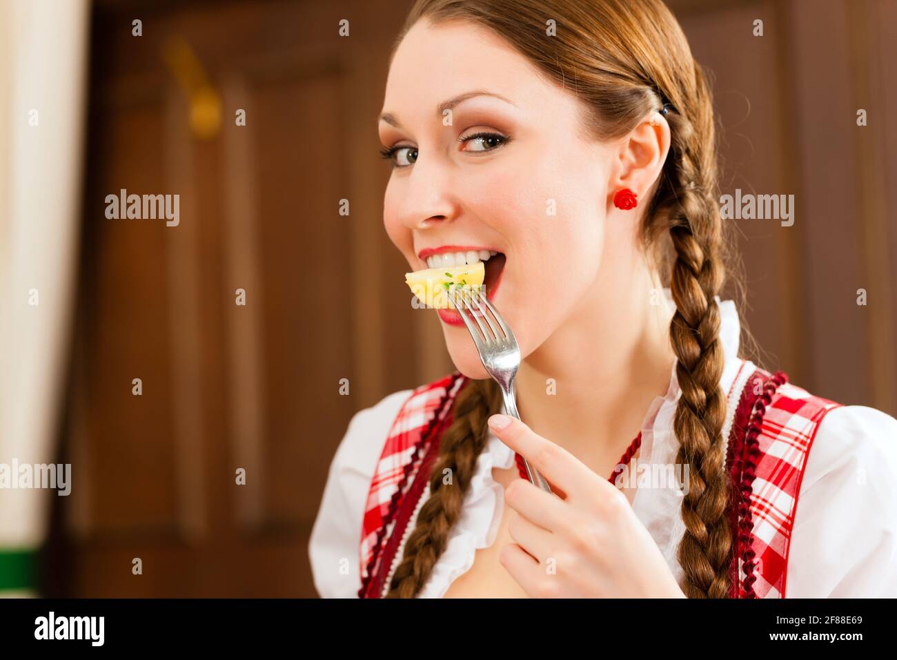 Young woman in traditional Bavarian Tracht eats in restaurant potatoes Stock Photo