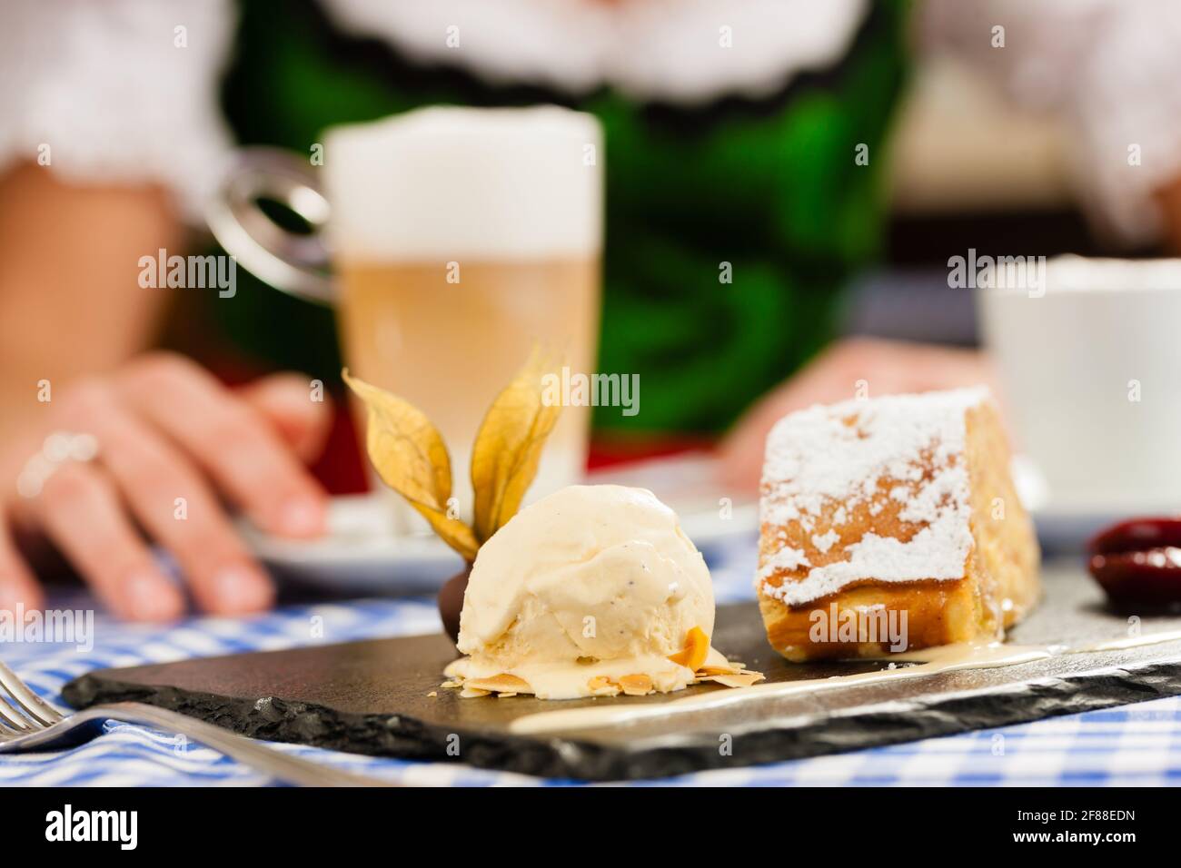 Young woman in traditional Bavarian Tracht in restaurant or pub eating dessert and drinking coffee, close-up Stock Photo