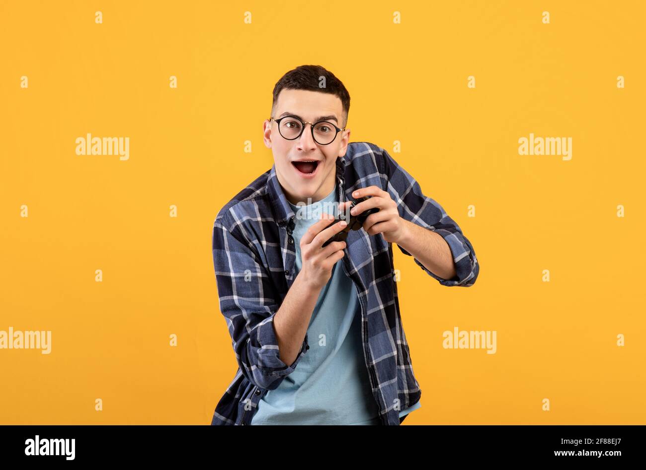 Excited young guy with joystick playing online video game on orange studio background Stock Photo