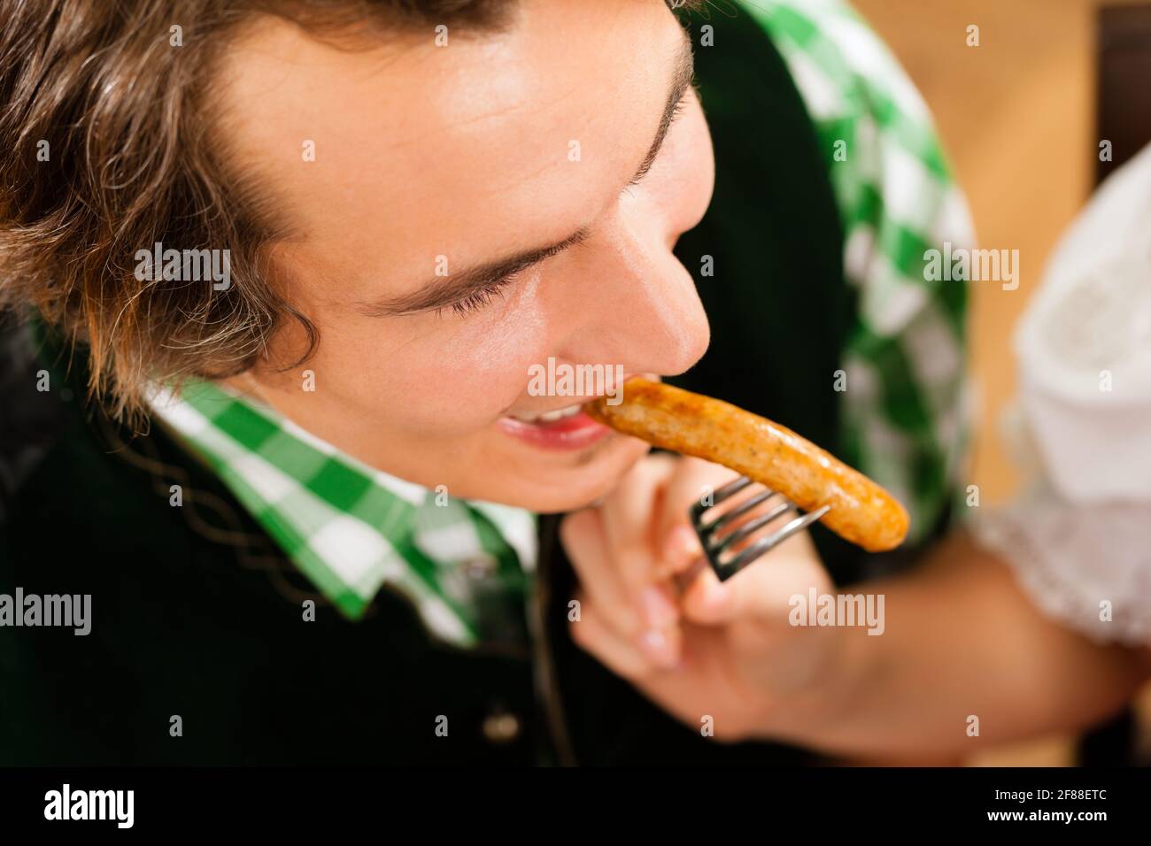 Young man in traditional clothes - loden suit - eating sausage in restaurant or pub or get feeded, close-up Stock Photo