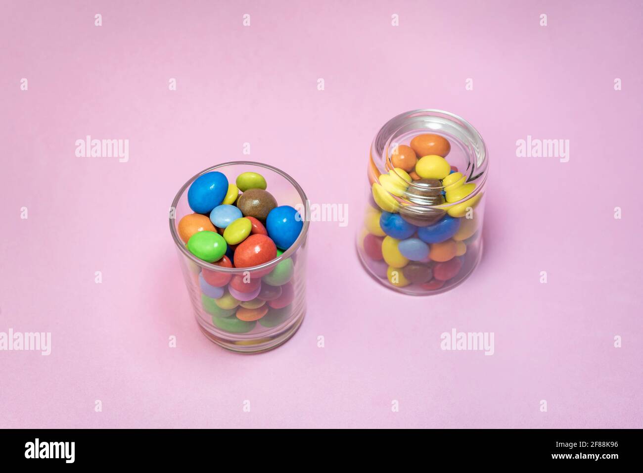 Multicolored chocolate candies in two glass on pink background.Closeup view of creative colorful sweets background concept with copy space for text. Stock Photo