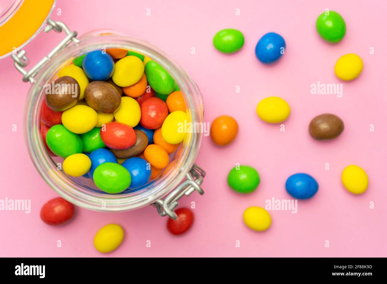 Multicolored chocolate candies in glass jar on pink background.Top view colorful sweets background concept. Stock Photo