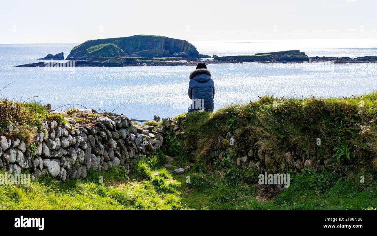 Person sat on dry stone wall looking out to sea. Stock Photo