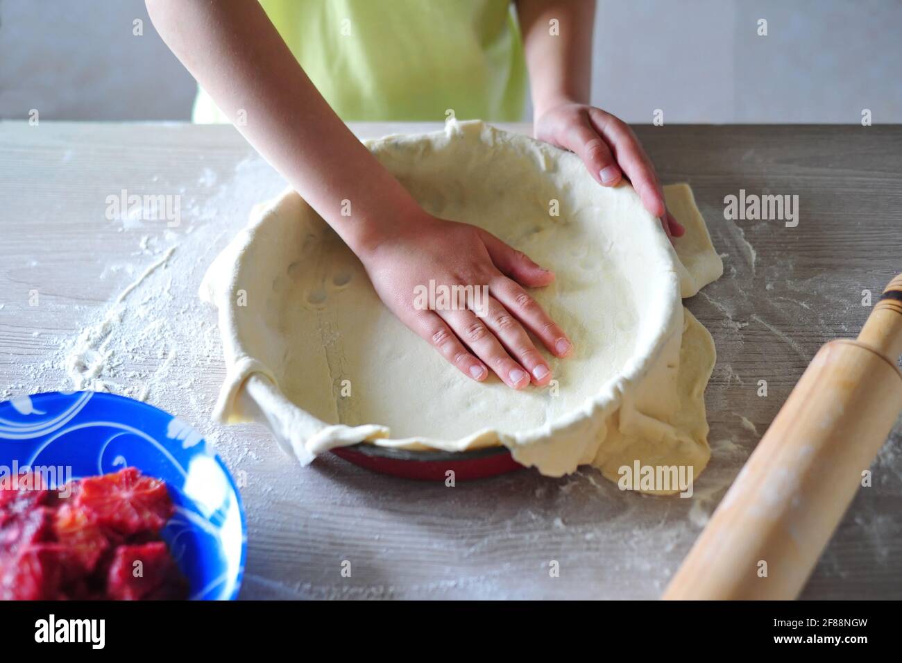 Cute little boy prepares a pie in the kitchen. The child rolls out the dough. Stock Photo