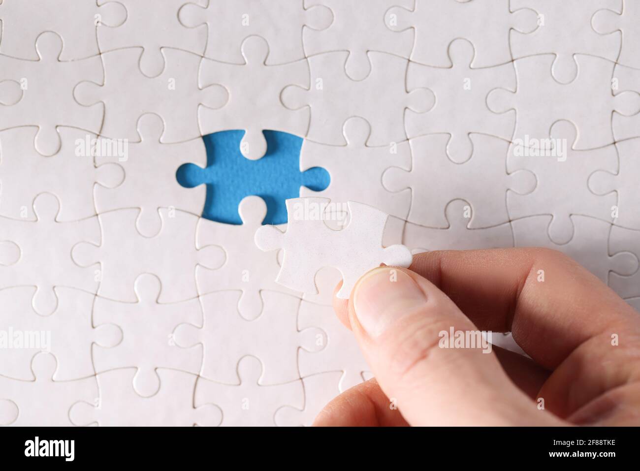 Man inserting last piece into white puzzle closeup Stock Photo