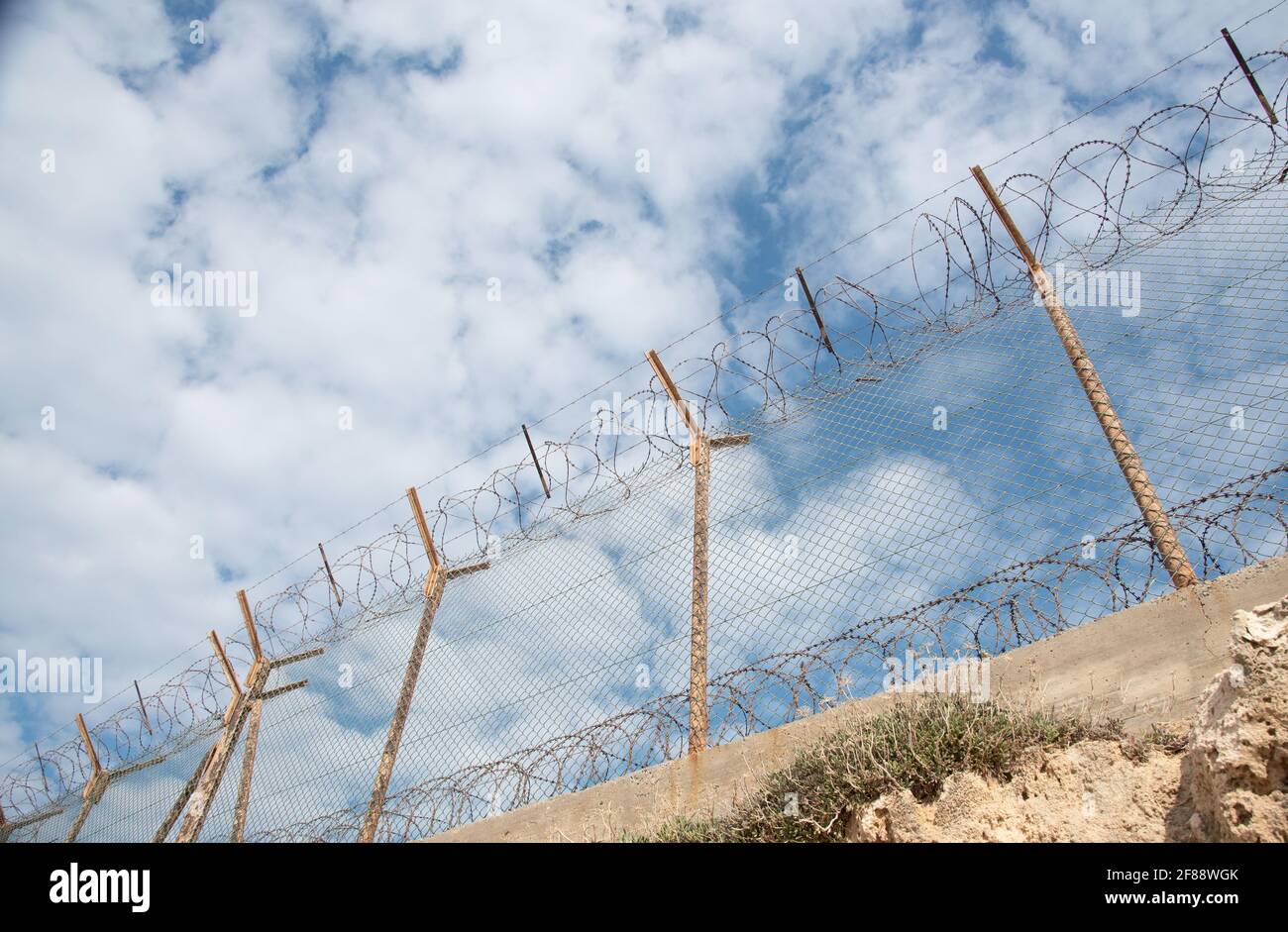 Security fence with barbed wire against a blue cloudy sky Stock Photo