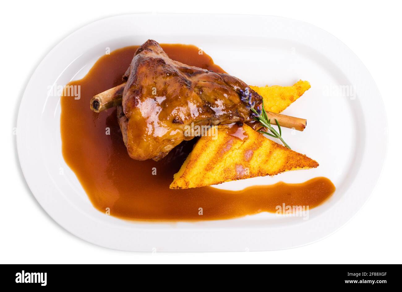Fried lamb shank with polenta and covered with red sauce. Isolated on a white background. Stock Photo