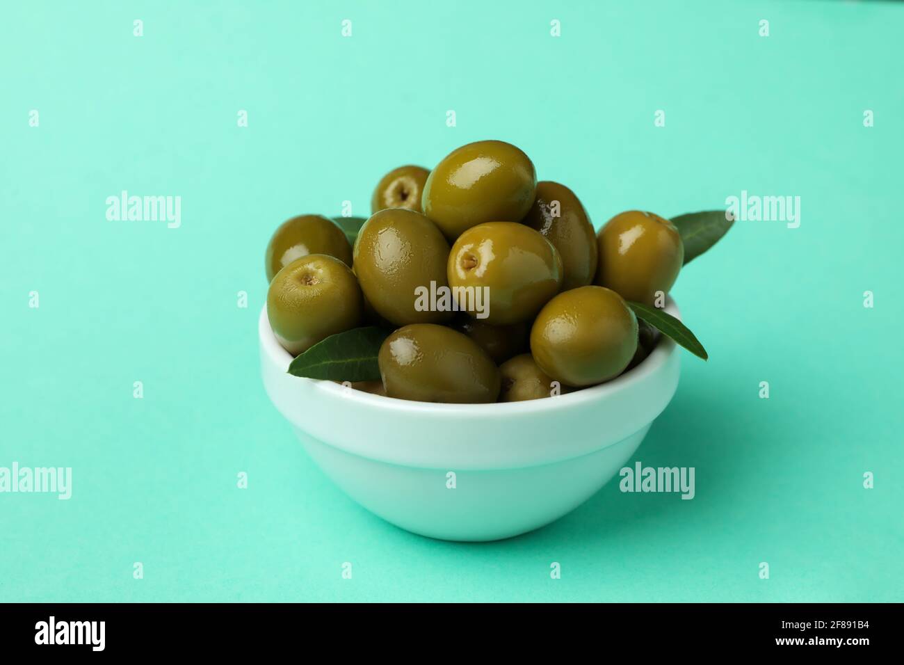 Bowl of green olives and leaves on mint background Stock Photo Alamy