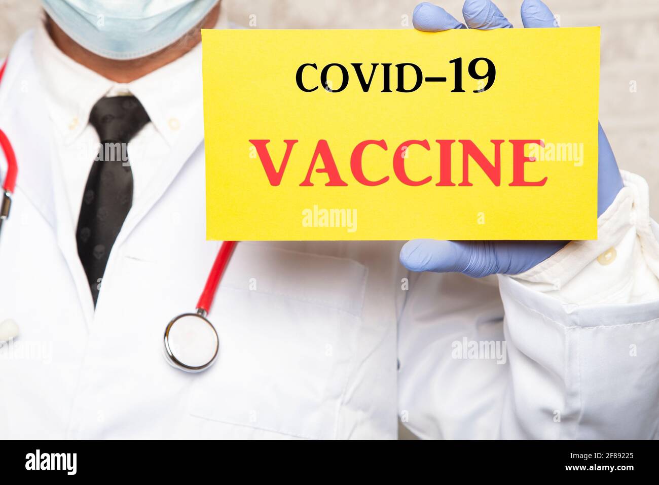 Close up of a male doctor in gloves holding a sign with the text COVID-19 VACCINE Stock Photo