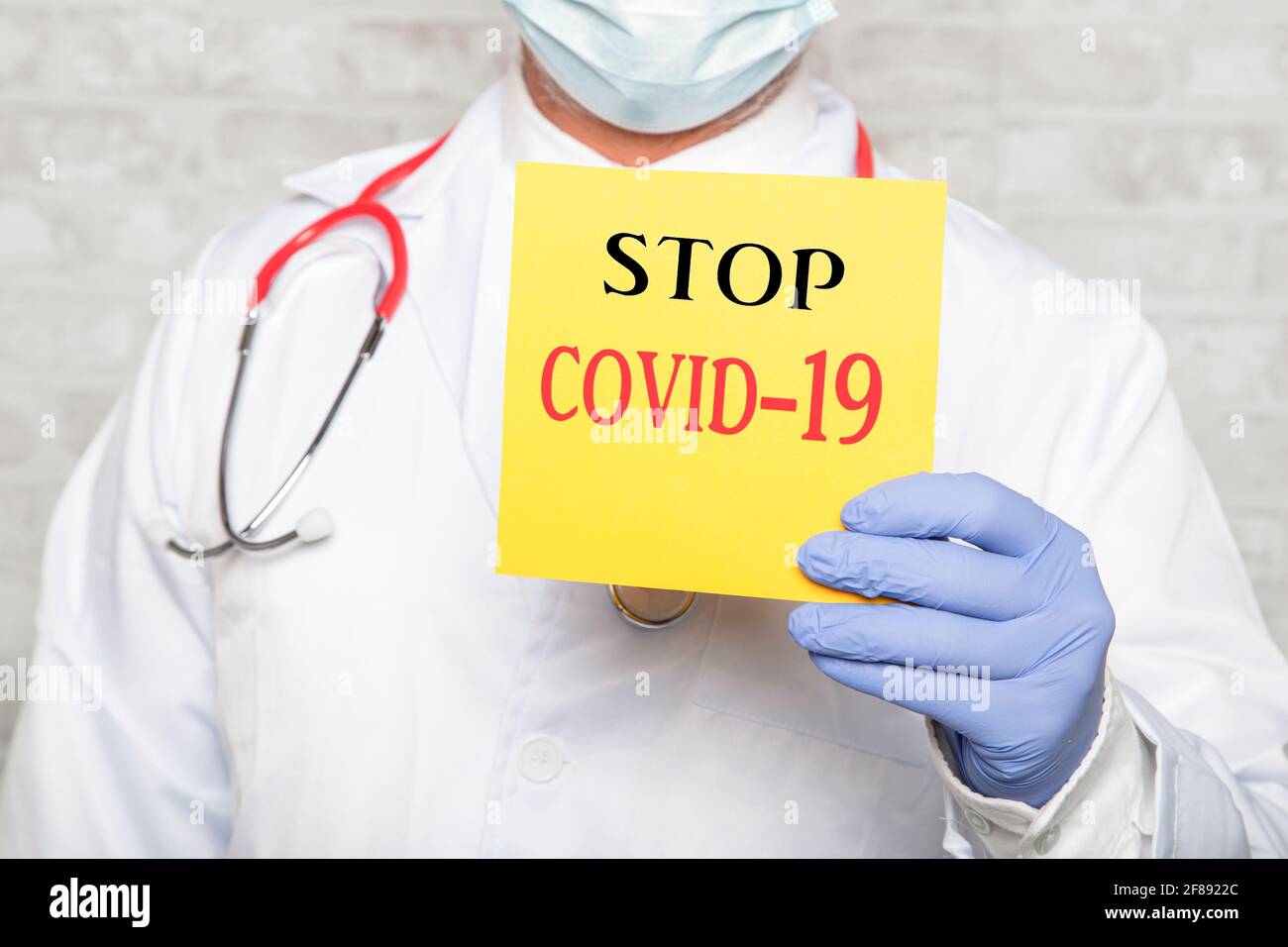 Portrait of doctor in gloves holding a sign with the text STOP COVID-19 Stock Photo
