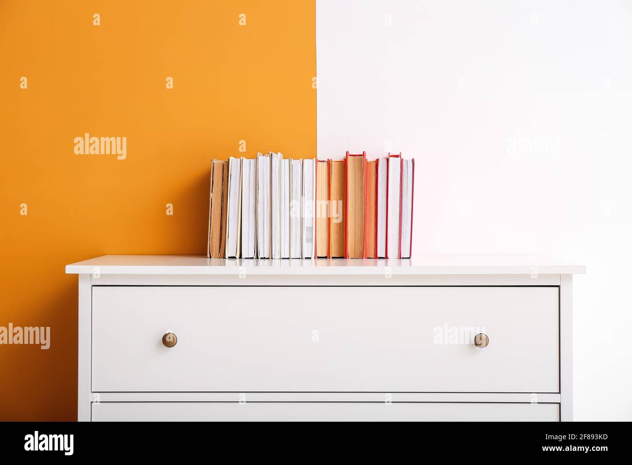 Chest of drawers with books on color background Stock Photo - Alamy