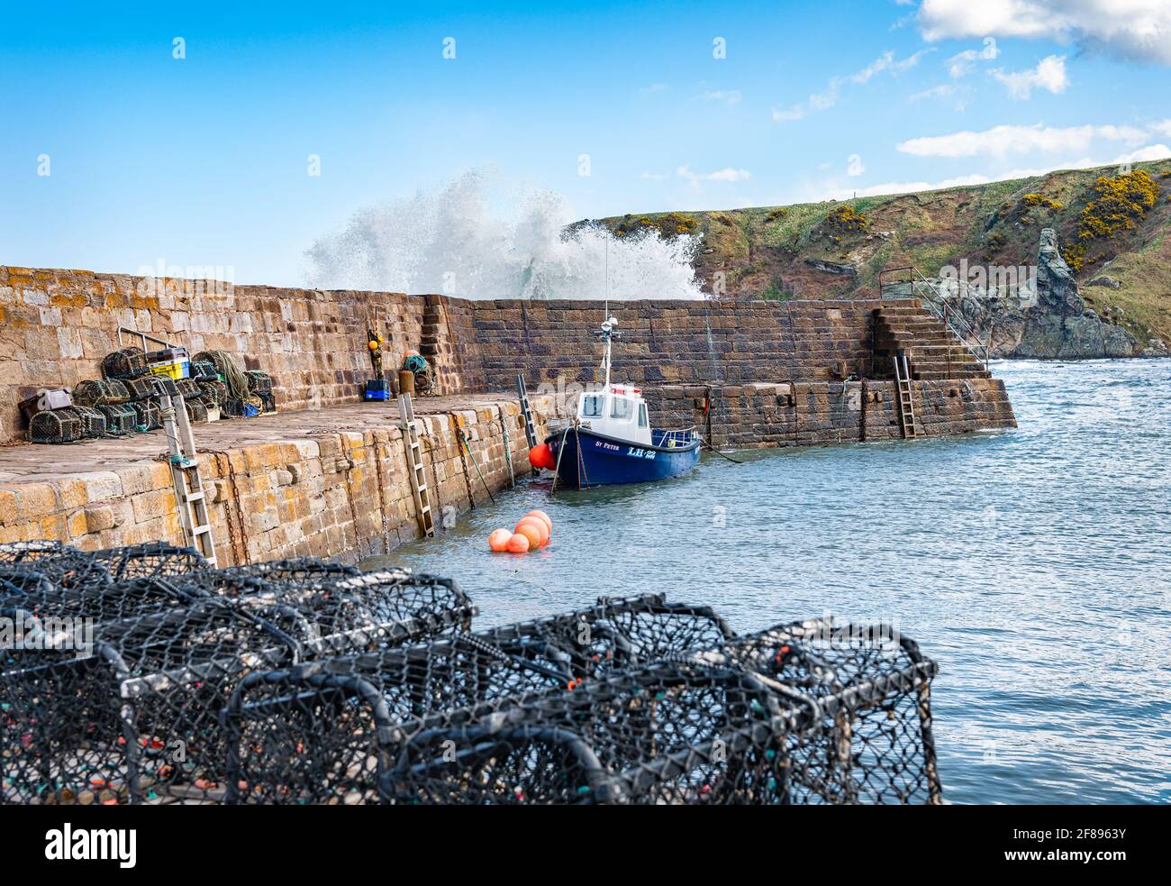 A fishing boat with a wave coming over the harbour wall at Cove Harbour