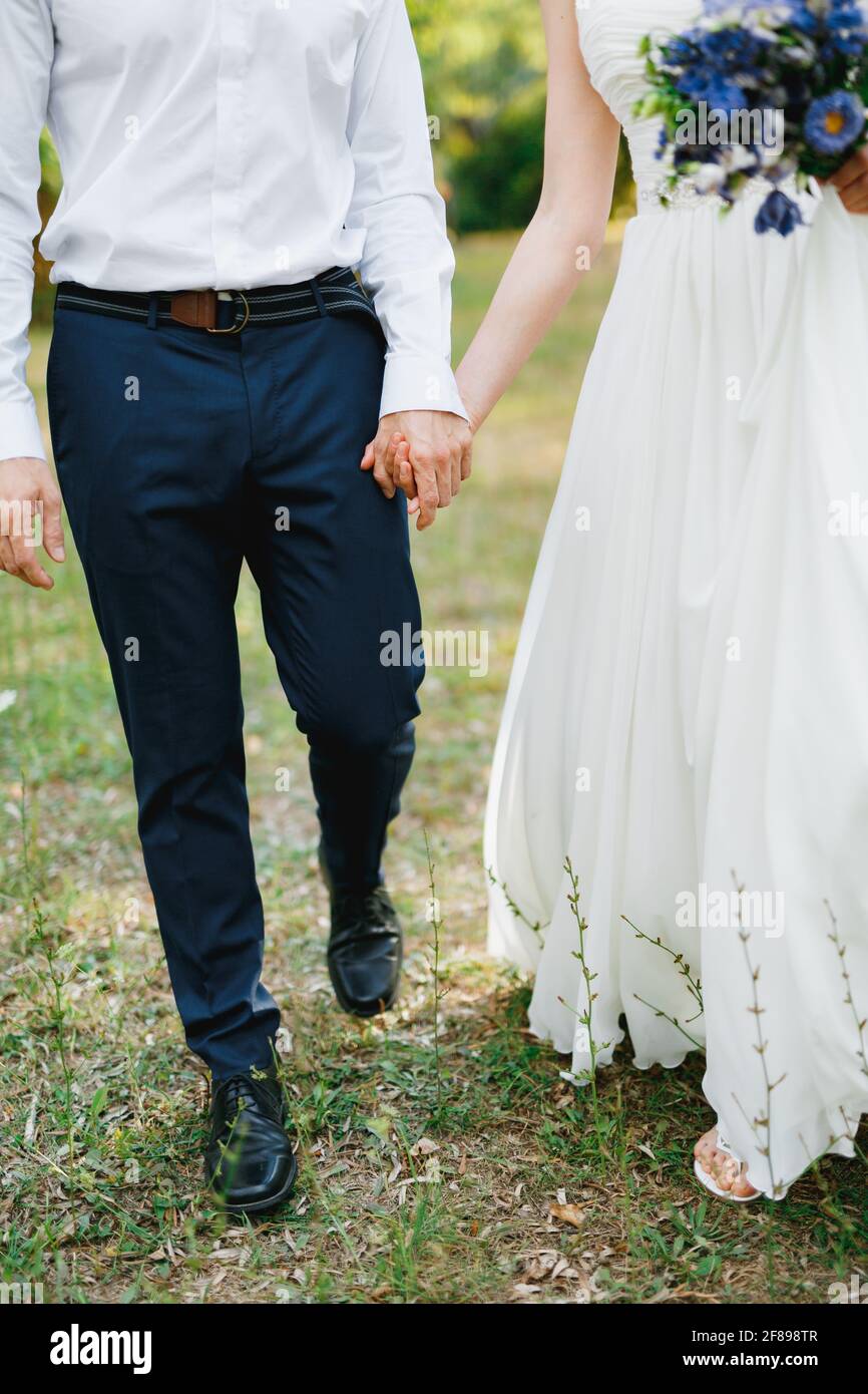 Bride with a bouquet of blue flowers and the groom walk side by side in the olive grove and hold hands Stock Photo