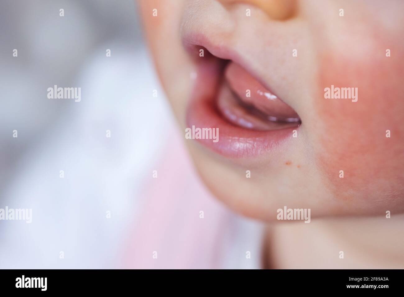 A macro portrait of a baby mouth with the first two small white teeth coming out of the gums. The little child has a smile on its face. The two teeth Stock Photo