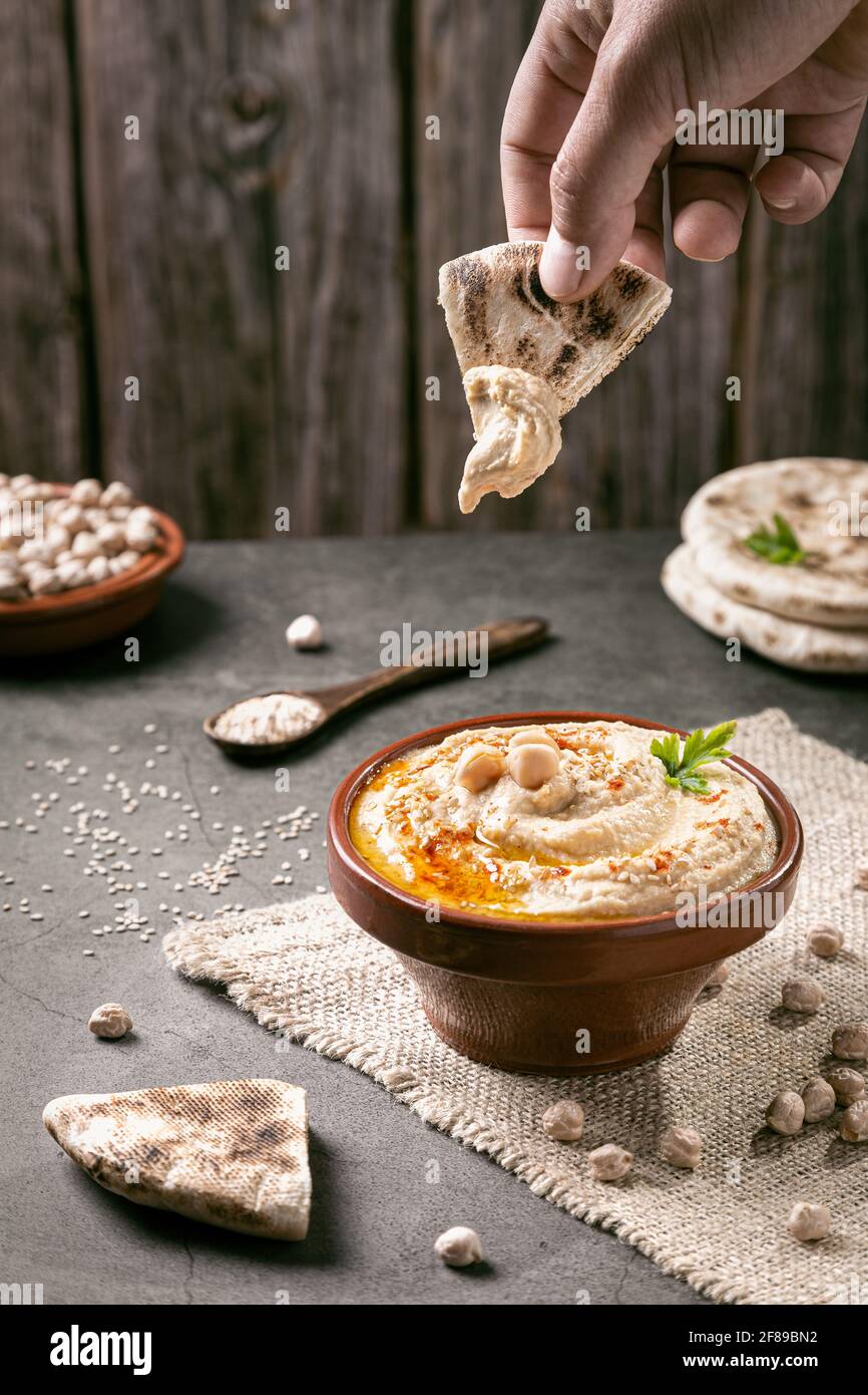 Hand dipping pita bread in hummus on dark background vertical format