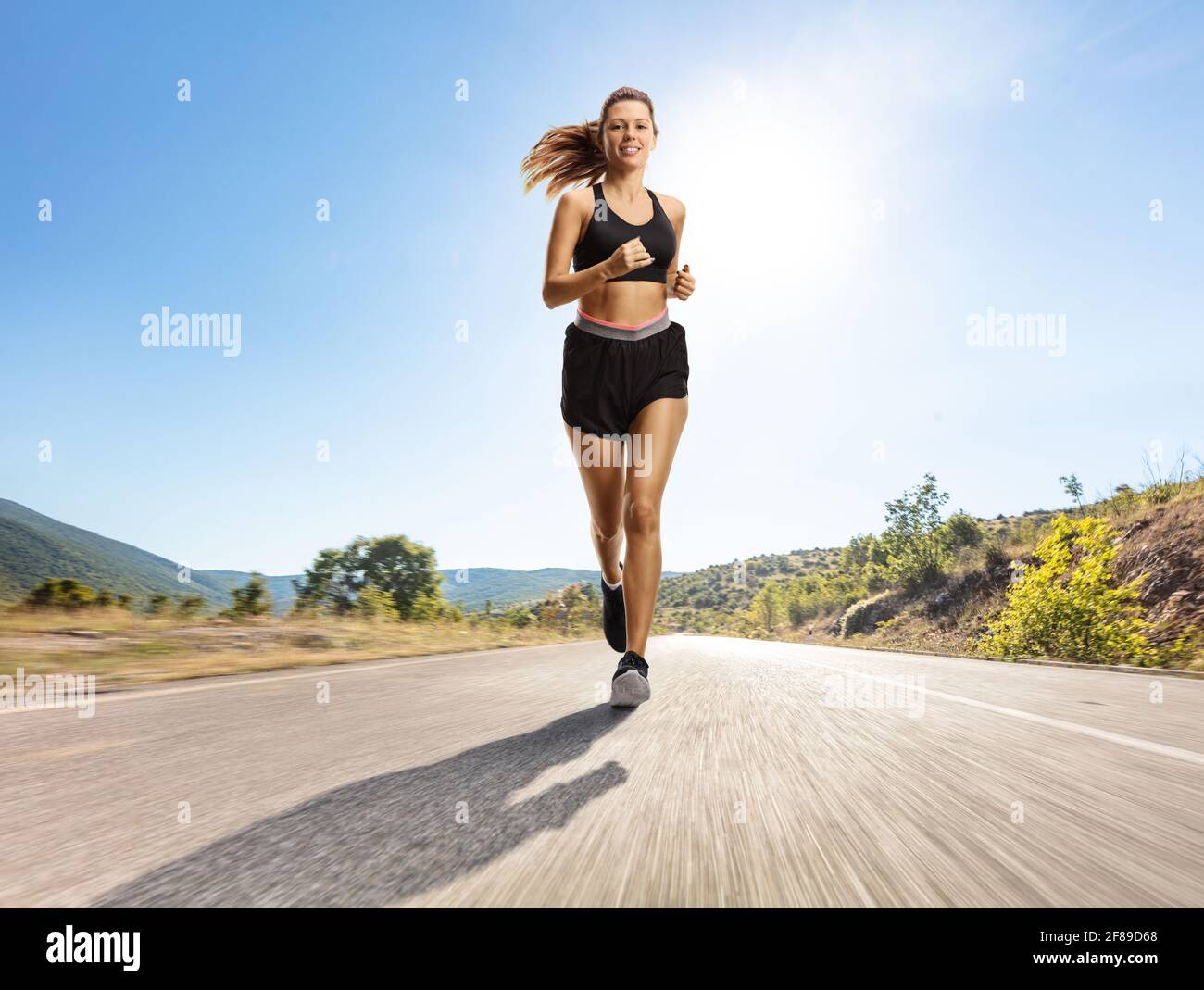 Full length portrait of a young woman jogging on a road towards the camera Stock Photo