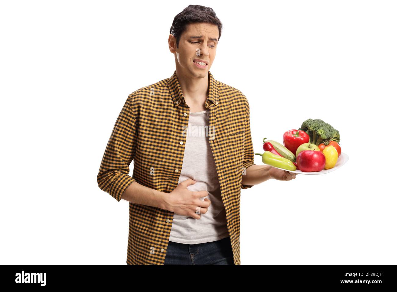 Young man with a stomach ache holding a plate of vegetables isolated on white background Stock Photo