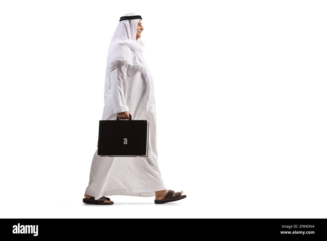 Full length profile shot of an arab man in a white thobe carrying a briefcase and walking isolated on white background Stock Photo