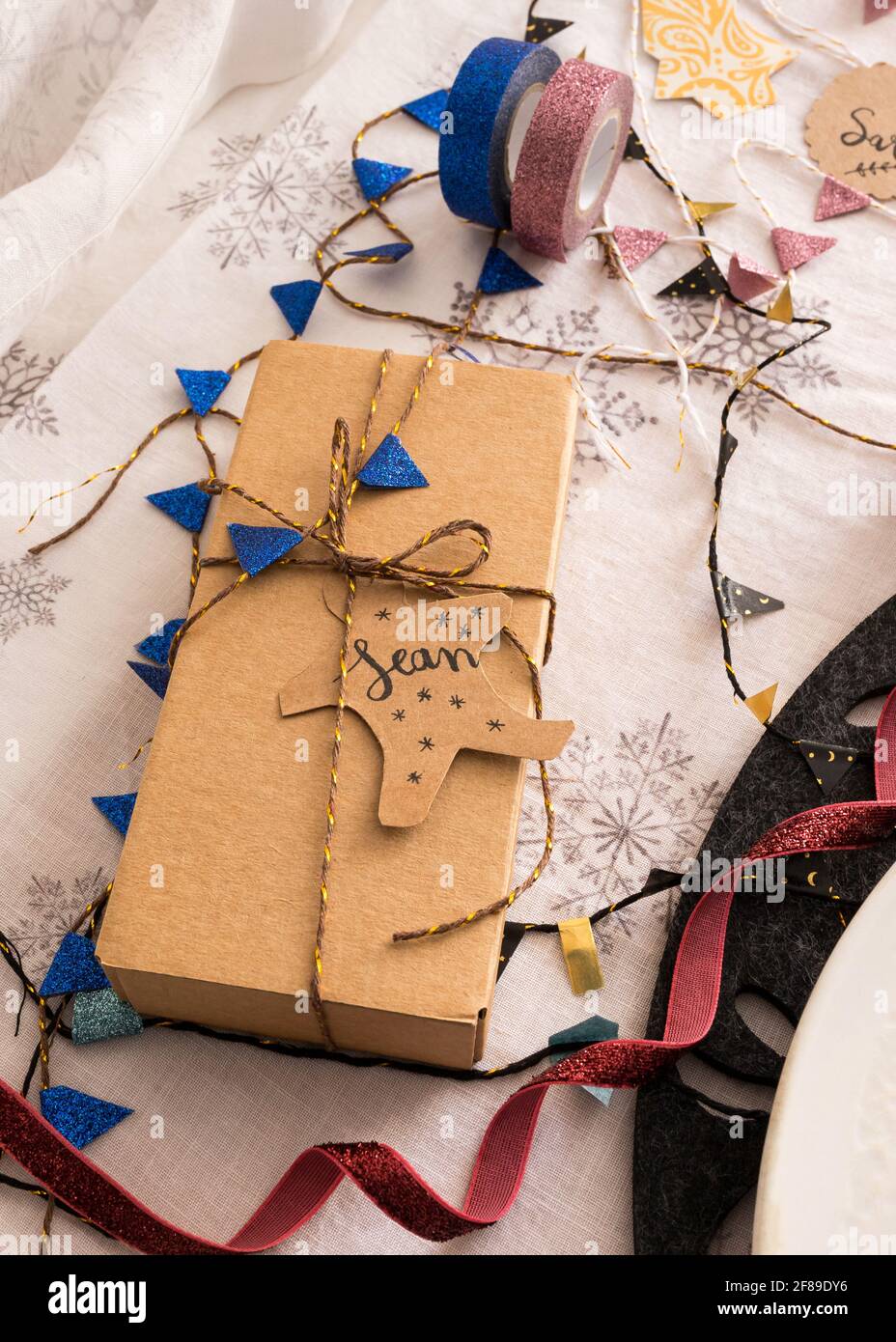Christmas gift box tied with golden ribbon and a blue garland. The name Sean is on the tag. Stock Photo
