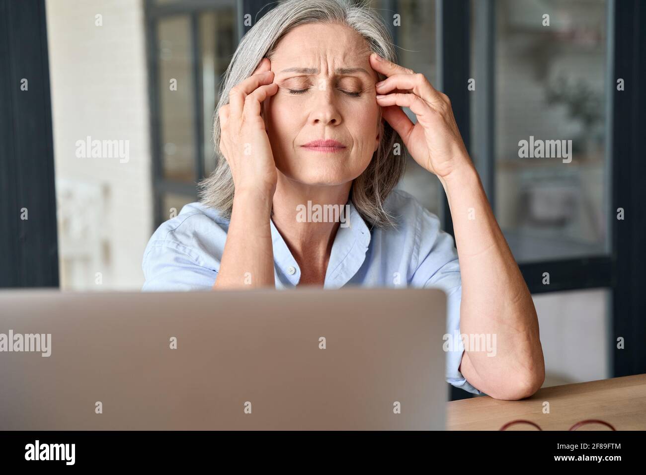 Stressed senior 60s aged massaging head at home office, suffering on workplace. Stock Photo