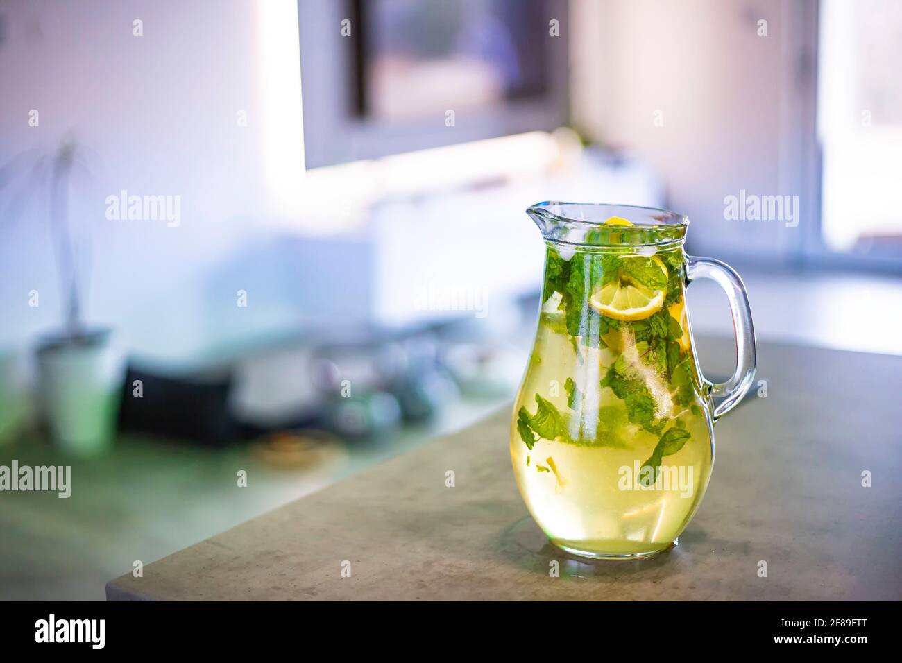 Ice cold lemonade with mint and lemon. The pitcher is standing on the kitchen counter. Background is blurred. Stock Photo