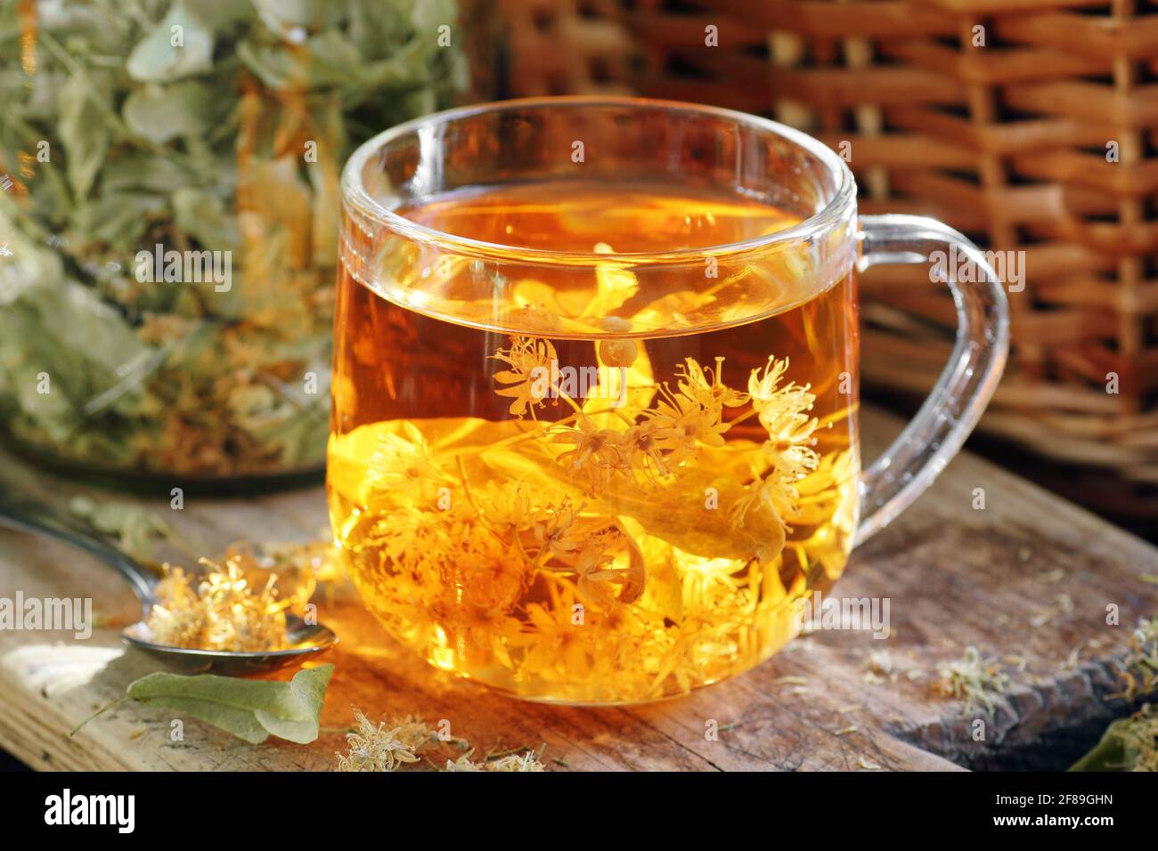 Linden herbal tea with flowers in a glass cup on wooden rustic board with lime blossom dry herb nearby, closeup, drink for relaxation, mental health, Stock Photo