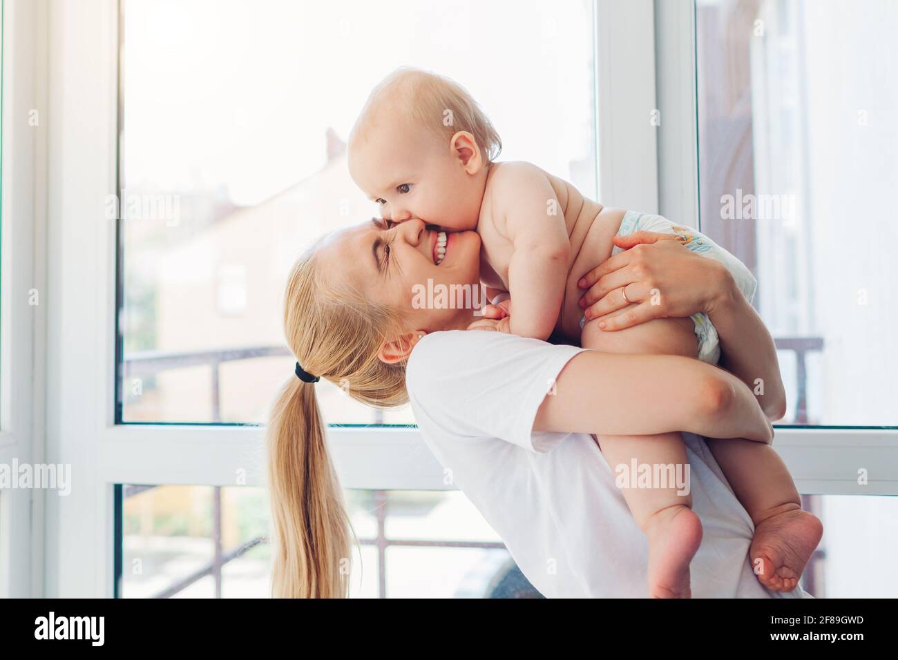 Mother's day. Young mother holding and hugging newborn baby son at home. Family relaxing on balcony. Infant wearing diaper. Stock Photo
