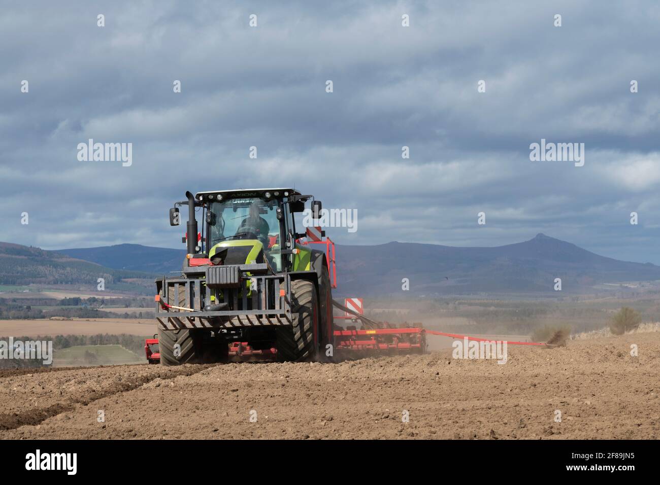 A Tractor and Disc Seed Drill Sowing Barley on a Sunny Spring Afternoon in an Aberdeenshire Field in Sight of Bennachie Stock Photo