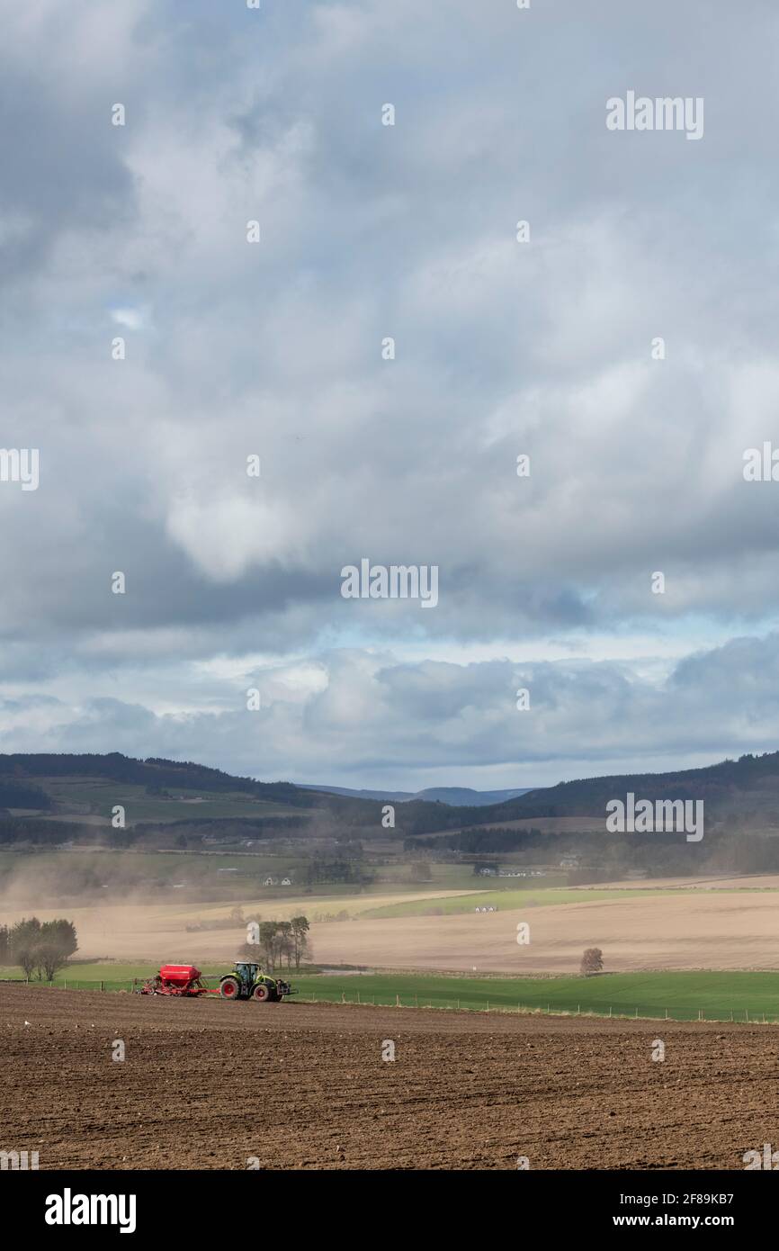 A View Over Windswept Countryside in Aberdeenshire in Spring with a Farmer Planting a Crop in the Field in the Foreground Stock Photo