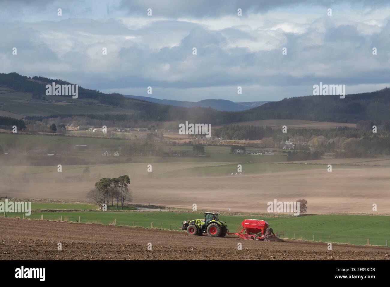 A View of the Barren Aberdeenshire Countryside Towards the Suie in Spring with a Farmer Sowing a Crop on a Windy Afternoon Stock Photo