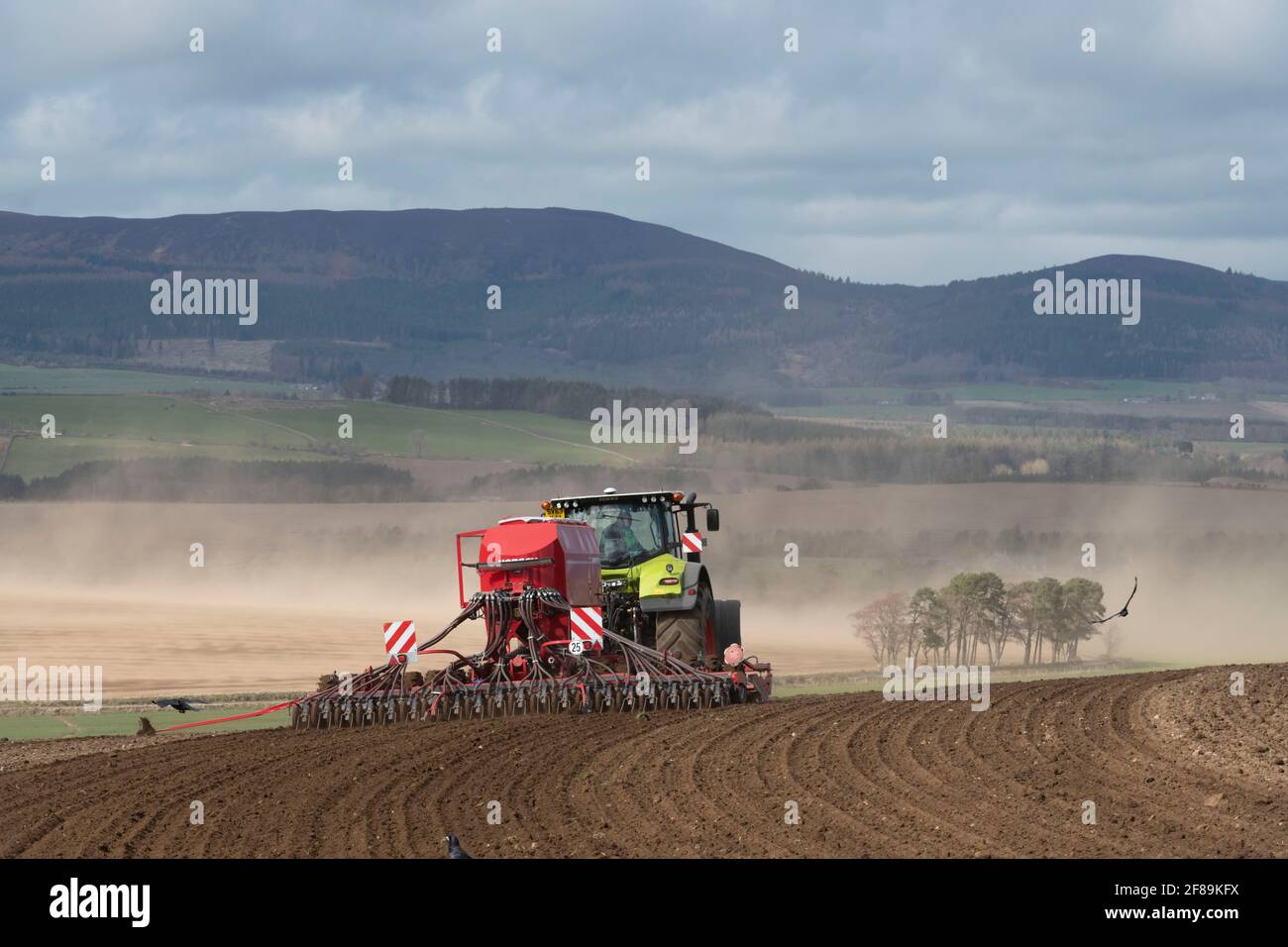A Farmer Planting Seed in Rural Scotland as Wind Blows Soil From a Field in the Background Stock Photo