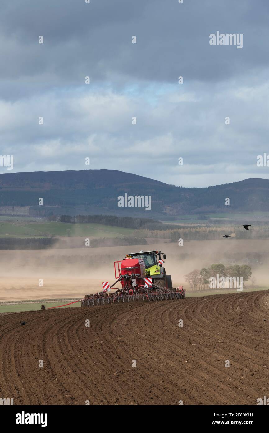 A Disc Seed Drill Sowing Grain with Wind Blowing Soil From a Field Visible in the Distance Stock Photo