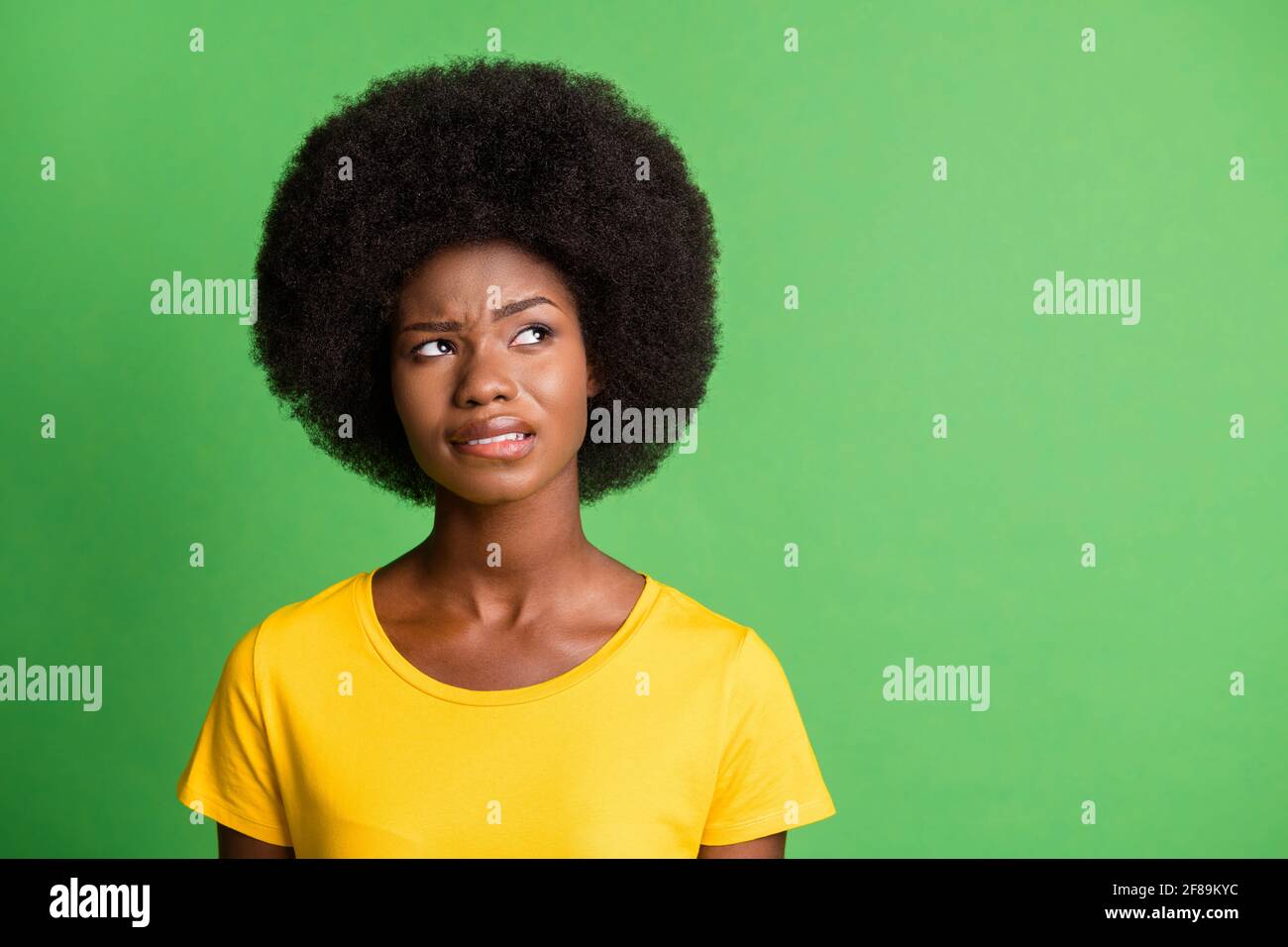 Photo portrait of curious woman biting lip looking empty space isolated on bright green color background Stock Photo