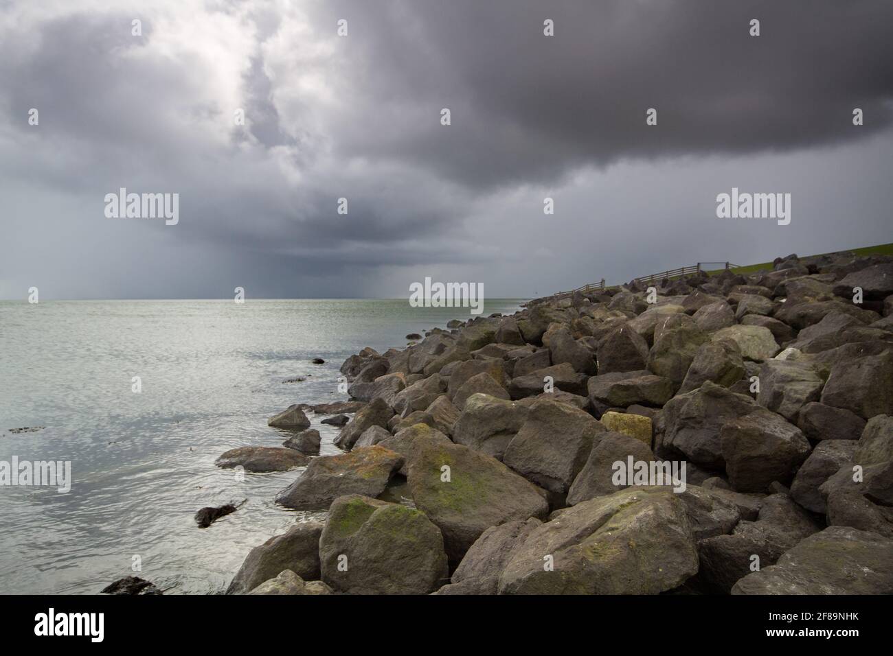 Toe protection of a solid sea dike, made of heavy boulders, under dark, threatening sky Stock Photo