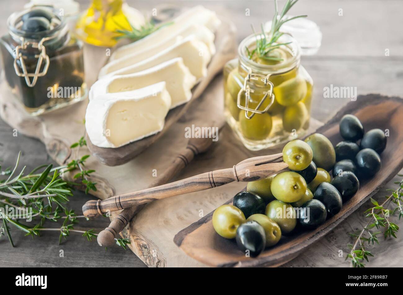 Green and black olives in glass jars with white soft brie cheese and